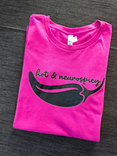 Load image into Gallery viewer, A folded hot pink t-shirt with a black graphic of a chili pepper and the text 'hot &amp; neurospicy' printed on the front, laid flat on a dark gray textured surface.